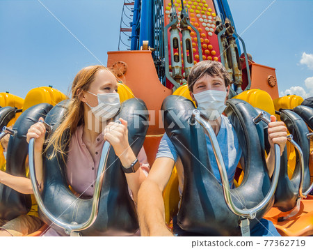 Family wearing a medical mask during COVID-19 coronavirus at an amusement park Family wearing a medical mask during COVID-19 coronavirus at an amusement park 77362719
