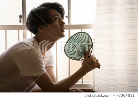 一個男人在炎熱的天氣裡在房間裡看智能手機 77364031