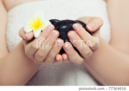 Spa concept with black massage stones and tropical flower in beautiful woman hands 77364616