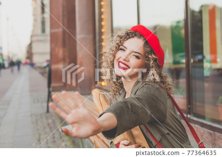 Happy young woman wearing red french beret waving hello 77364635