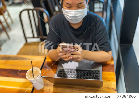 Woman wearing disposable mask while using smartphone in coffee shop Woman wearing disposable mask while using smartphone in coffee shop 77364860