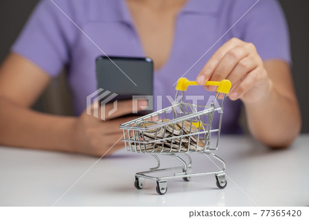 Woman pushing shopping cart full of coins and holding phone, concept investment fund finance and business. 77365420