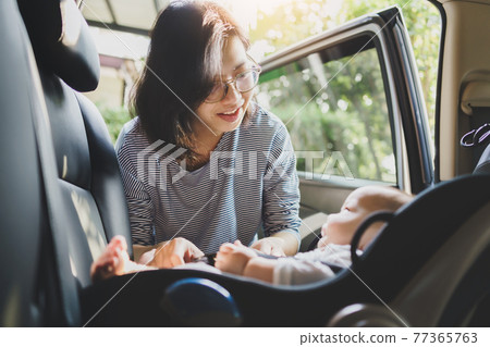 Asian Mother helping her little baby boy son to fasten belt on his car seat 77365763