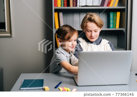 Front view of brother interferes to kid boy ability to play on laptop studying online and communicating with friends 77366148