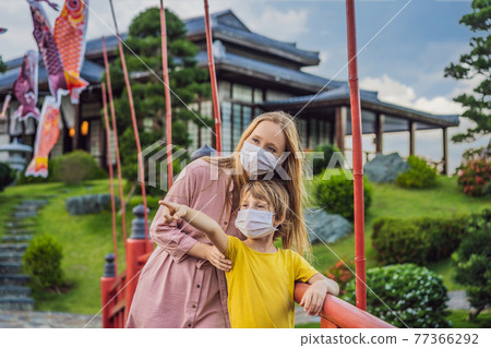 Mother and son travelers in medical mask looking at the Japanese traditional building. Tourists travel in Japan after the coronavirus epidemic 77366292