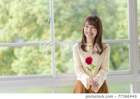 一個年輕女子在窗邊拿著一朵玫瑰 77366449