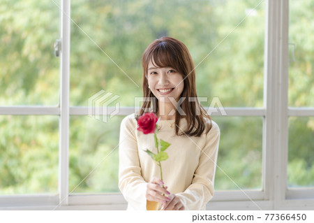 一個年輕女子在窗邊拿著一朵玫瑰 77366450