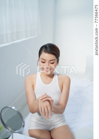 Young skin care woman applying body lotion on arm and shoulder at home 77366475