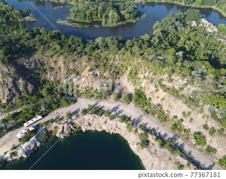 Rocky shore of the Radon Lake on a sunny summer morning. Aerial view of an old flooded granite quarry. A picturesque pond. 77367181