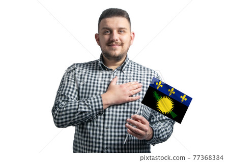 White guy holding a flag of Guadeloupe and holds his hand on his heart isolated on a white background With love to Guadeloupe White guy holding a flag of Guadeloupe and holds his hand on his heart isolated on a white background With love to Guadeloupe 77368384