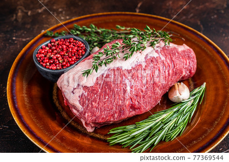 Raw round beef meat prime cut for roast on a rustic plate with herbs. Dark background. Top view Raw round beef meat prime cut for roast on a rustic plate with herbs. Dark background. Top view 77369544