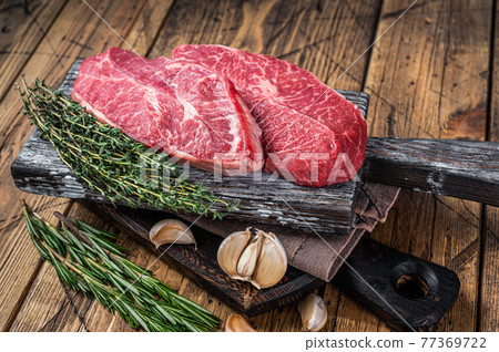 Raw Shoulder Top Blade beef meat steaks on a wooden butcher board with herbs. wooden background. Top View Raw Shoulder Top Blade beef meat steaks on a wooden butcher board with herbs. wooden background. Top View 77369722