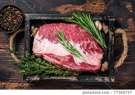 Raw brisket beef meat cut on a wooden tray with knife. Dark wooden background. Top view 77369737