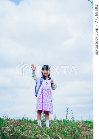 Little girl carrying a backpack and waving Little girl carrying a backpack and waving 77369892