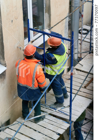 Workers erect scaffolding to repair the facade of a building Workers erect scaffolding to repair the facade of a building 77370097