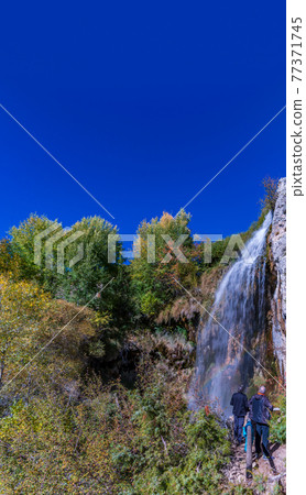 Unrecognizable people looking at the waterfall, blue sky Unrecognizable people looking at the waterfall, blue sky 77371745