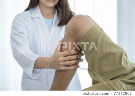 Female doctor hands doing physical therapy By extending the leg and knee of a male patient 77372901
