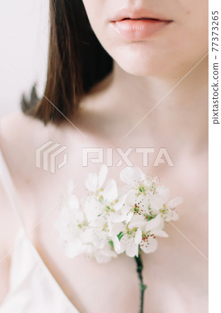 Young beautiful woman with flowers on white background. Tender pure portrait. Face skincare and health wellness, Natural makeup. Young beautiful woman with flowers on white background. Tender pure portrait. Face skincare and health wellness, Natural makeup. 77373265