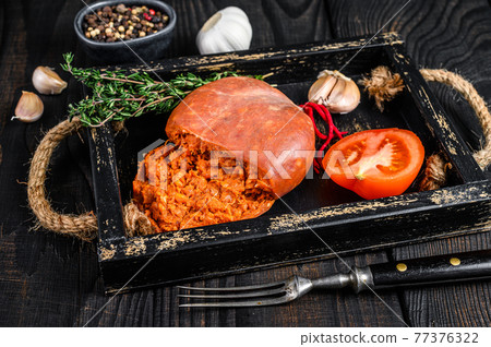 Mallorcan Sobrassada cured pork meat sausage in a wooden tray. Black wooden background. Top view 77376322