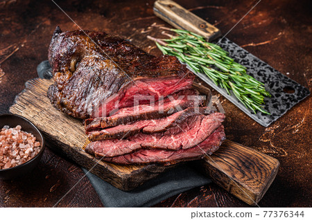 Roasted hanging tender or Onglet sliced beef meat steak on a butcher board with cleaver. Dark background. Top View 77376344