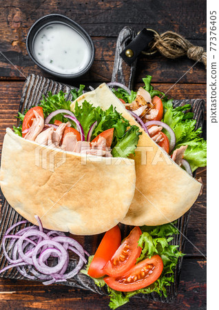 Greek gyros wrapped in pita breads with vegetables and sauce. Dark wooden background. Top view Greek gyros wrapped in pita breads with vegetables and sauce. Dark wooden background. Top view 77376405