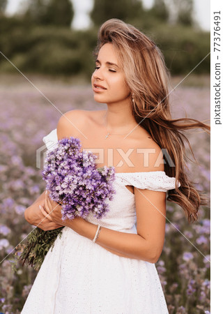 girl in a white dress with a bouquet of purple flowers in a field girl in a white dress with a bouquet of purple flowers in a field 77376491