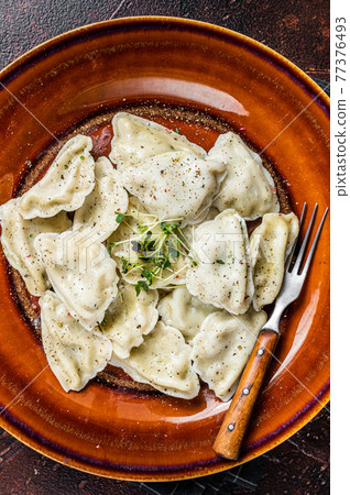 Polish Pierogi Dumplings with potato in a plate with herbs and butter. Dark background. Top View 77376493