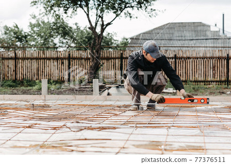 male worker measures the construction level of rebar for the foundation male worker measures the construction level of rebar for the foundation 77376511