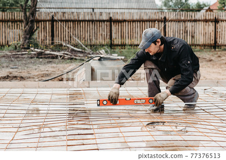 male worker measures the construction level of rebar for the foundation male worker measures the construction level of rebar for the foundation 77376513