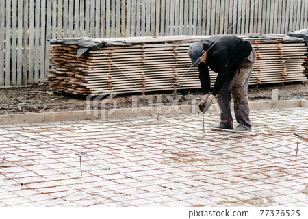 male construction worker prepares rebar for the foundation of the construction of a house male construction worker prepares rebar for the foundation of the construction of a house 77376525