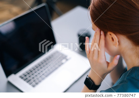 Close-up back view of tired frustrated young female doctor in blue medical uniform massaging temples, suffering from headache 77380747