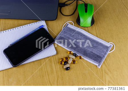 Laptop with mouse, smartphone, notebook, pen, medical mask and vitamins on a desk. Top view. Concept of homeschooling and working from home during quarantine. Stay at home Laptop with mouse, smartphone, notebook, pen, medical mask and vitamins on a desk. Top view. Concept of homeschooling and working from home during quarantine. Stay at home 77381361