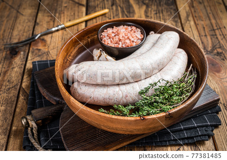 Raw Munich traditional white sausages in a wooden plate with herbs. wooden background. Top view 77381485