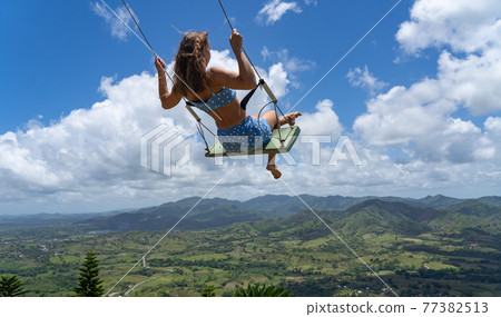Young woman on the rope swing with sky and mountains background. Concept of freedom and happiness  77382513