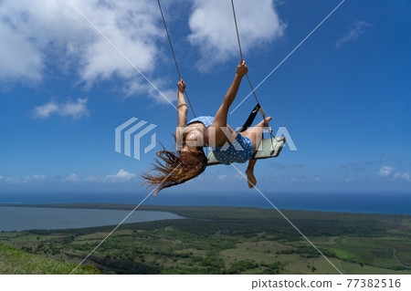 Young beautiful caucasian woman on the rope swing with sea and sky background. Concept of Vacation and carefree lifestyle 77382516
