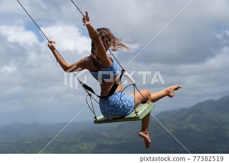 Young woman on the rope swing with sky and mountains background. Concept of freedom and happiness  77382519