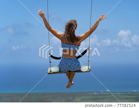 Young beautiful caucasian woman on the rope swing with sea and sky background. Concept of Vacation and travel  77382524