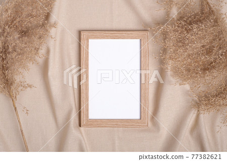Picture frame with blank paper card mockup near to pampas dry grass on beige neutral colored textile Picture frame with blank paper card mockup near to pampas dry grass on beige neutral colored textile 77382621