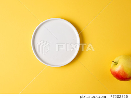 white plate and apple on yellow background 77382826