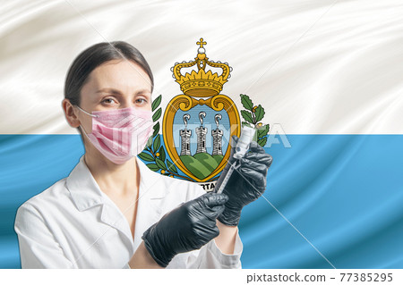 Girl doctor prepares vaccination against the background of the San Marino flag. Vaccination concept San Marino 77385295