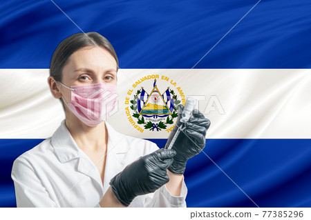 Girl doctor prepares vaccination against the background of the El Salvador flag. Vaccination concept El Salvador 77385296