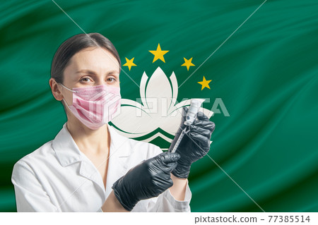 Girl doctor prepares vaccination against the background of the Macau flag. Vaccination concept Macau Girl doctor prepares vaccination against the background of the Macau flag. Vaccination concept Macau 77385514