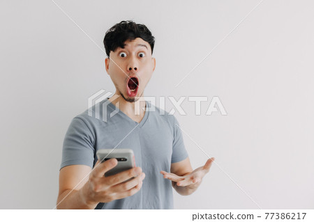 Wow and surprised face of man hold a smartphone isolated on white wall. Wow and surprised face of man hold a smartphone isolated on white wall. 77386217