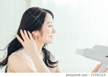 A woman using a hair dryer 77391314