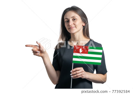 Happy young white woman holding flag Abkhazia and points to the left isolated on a white background Happy young white woman holding flag Abkhazia and points to the left isolated on a white background 77392584