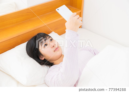 A girl watching a smartphone in bed 77394288