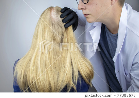 A doctor trichologist conducts a study of the hair of a blonde. Alopecia treatment. Hair loss, alopecia, itching, burning in the head, seborrhea or brittle ends 77395675