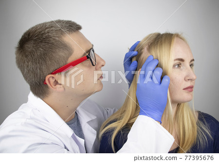 A doctor trichologist conducts a study of the hair of a blonde. Alopecia treatment. Hair loss, alopecia, itching, burning in the head, seborrhea or brittle ends 77395676