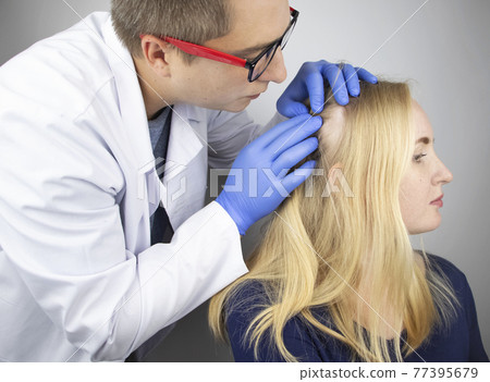 A doctor trichologist conducts a study of the hair of a blonde. Alopecia treatment. Hair loss, alopecia, itching, burning in the head, seborrhea or brittle ends 77395679