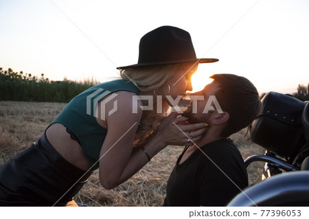 Bikers man and woman stopped at the side of the road to rest and kiss passionately. Photos of loving motorcyclists at sunset. The concept of freedom, brutality and passion 77396053